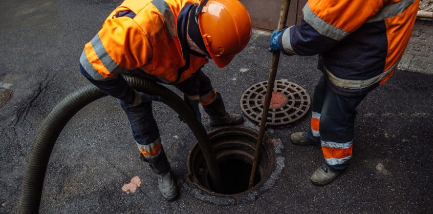 workers standing above a sewer and peering in