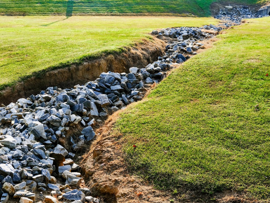 Rock-lined drainage ditch cutting through a grassy lawn.