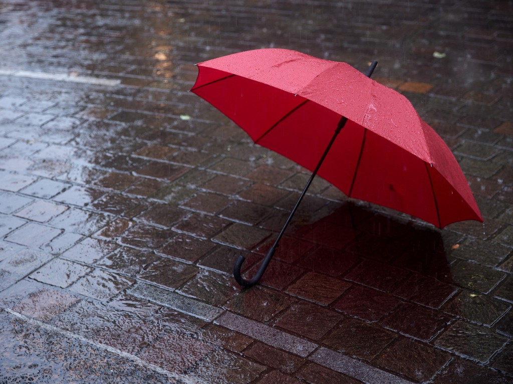 Red umbrella lying open on a rain-soaked brick pavement