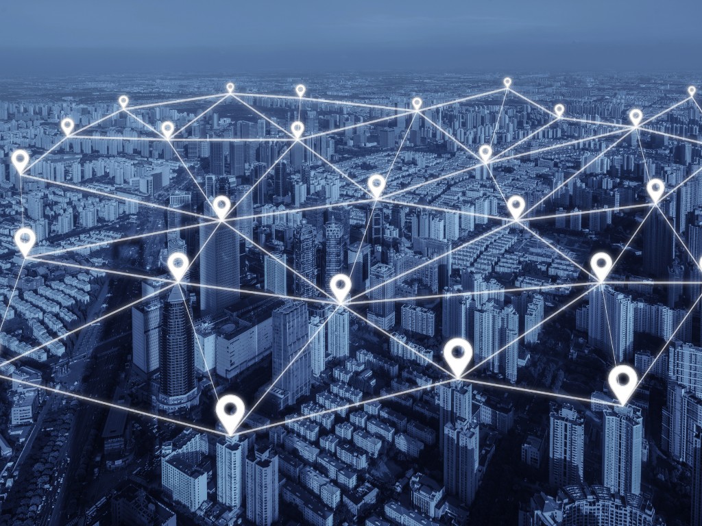 Aerial view of a city skyline overlaid with glowing map pins and connecting lines